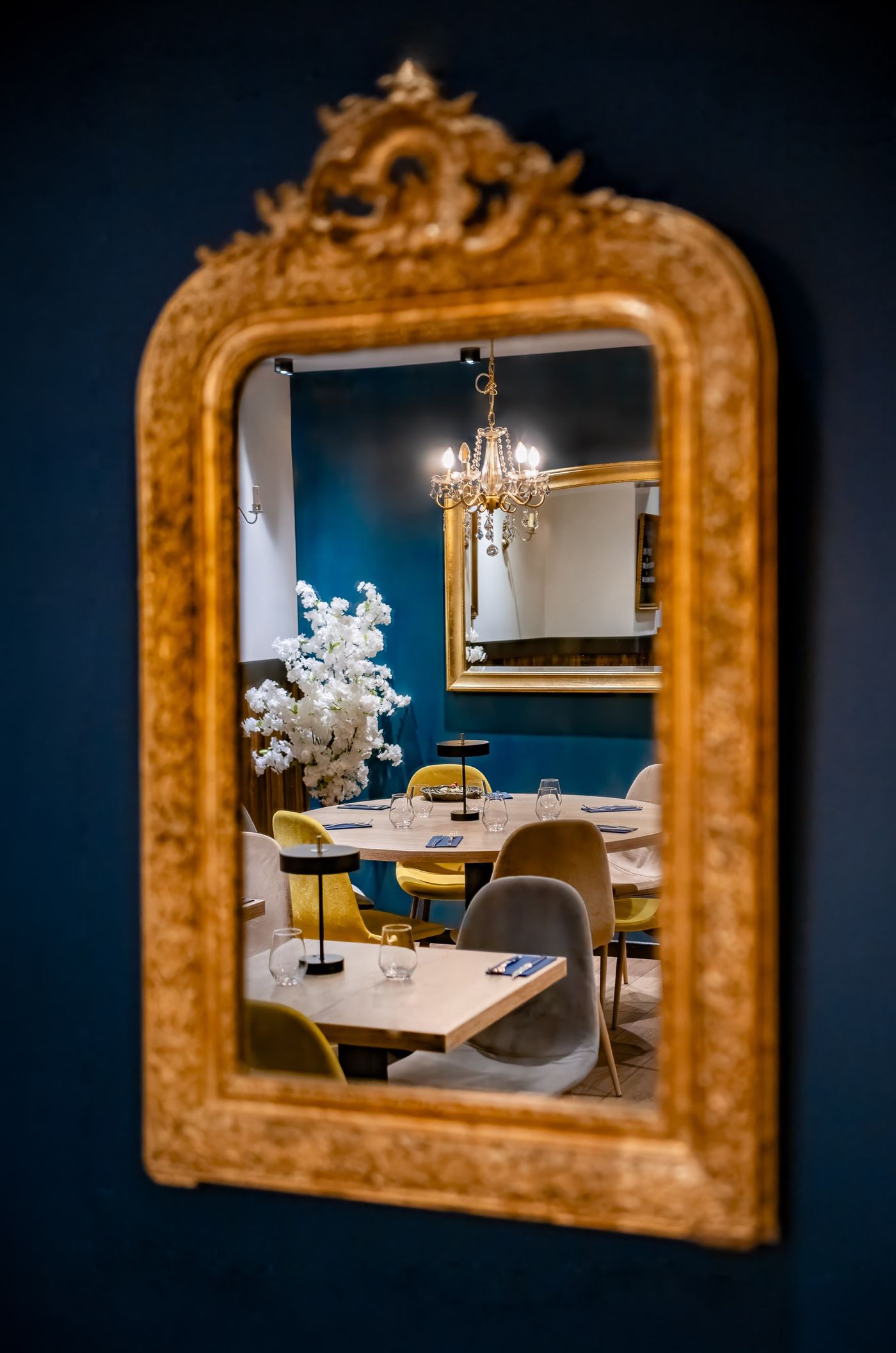 Miroir doré ancien reflétant la salle bleue et son lustre à pampilles