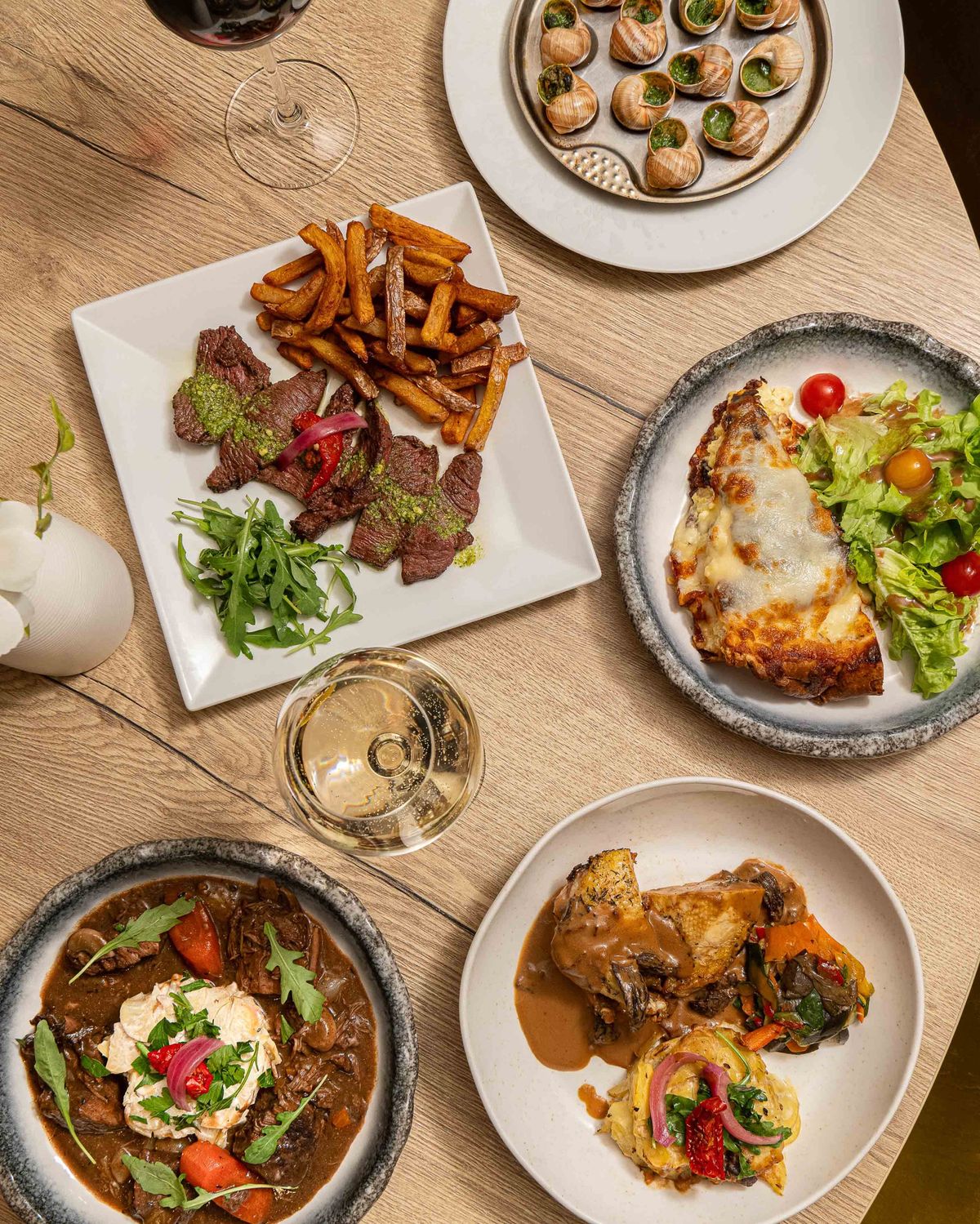Table laid at Brasserie Stanislas in Nancy, seen from above: snails, beef tagliata and chips, gratin and salad, bœuf bourguignon and chicken supreme